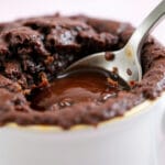 Close de um brownie de caneca com centro cremoso sendo servido com colher, sobremesa fácil pronta em 2 minutos.