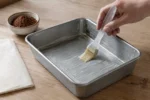Pincel espalhando manteiga em uma forma para brownie