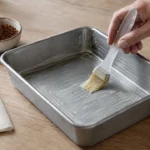 Pincel espalhando manteiga em uma forma para brownie