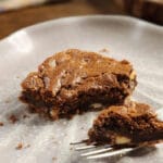 Brownie de chocolate com pedaços visíveis, servido em prato claro com garfo ao lado