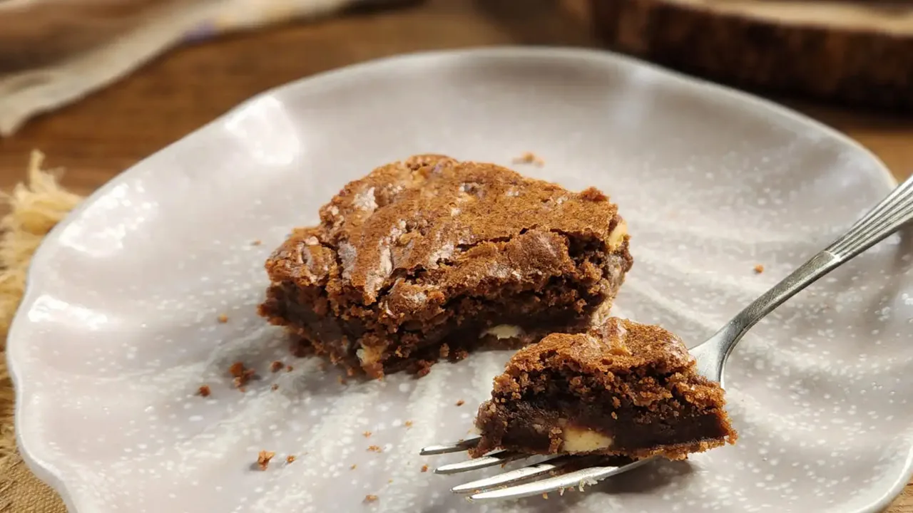 Brownie de chocolate com pedaços visíveis, servido em prato claro com garfo ao lado