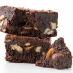 foto de três pedaços de brownie com nozes empilhados sobre fundo branco, destacando a textura densa e os pedaços crocantes de castanhas.