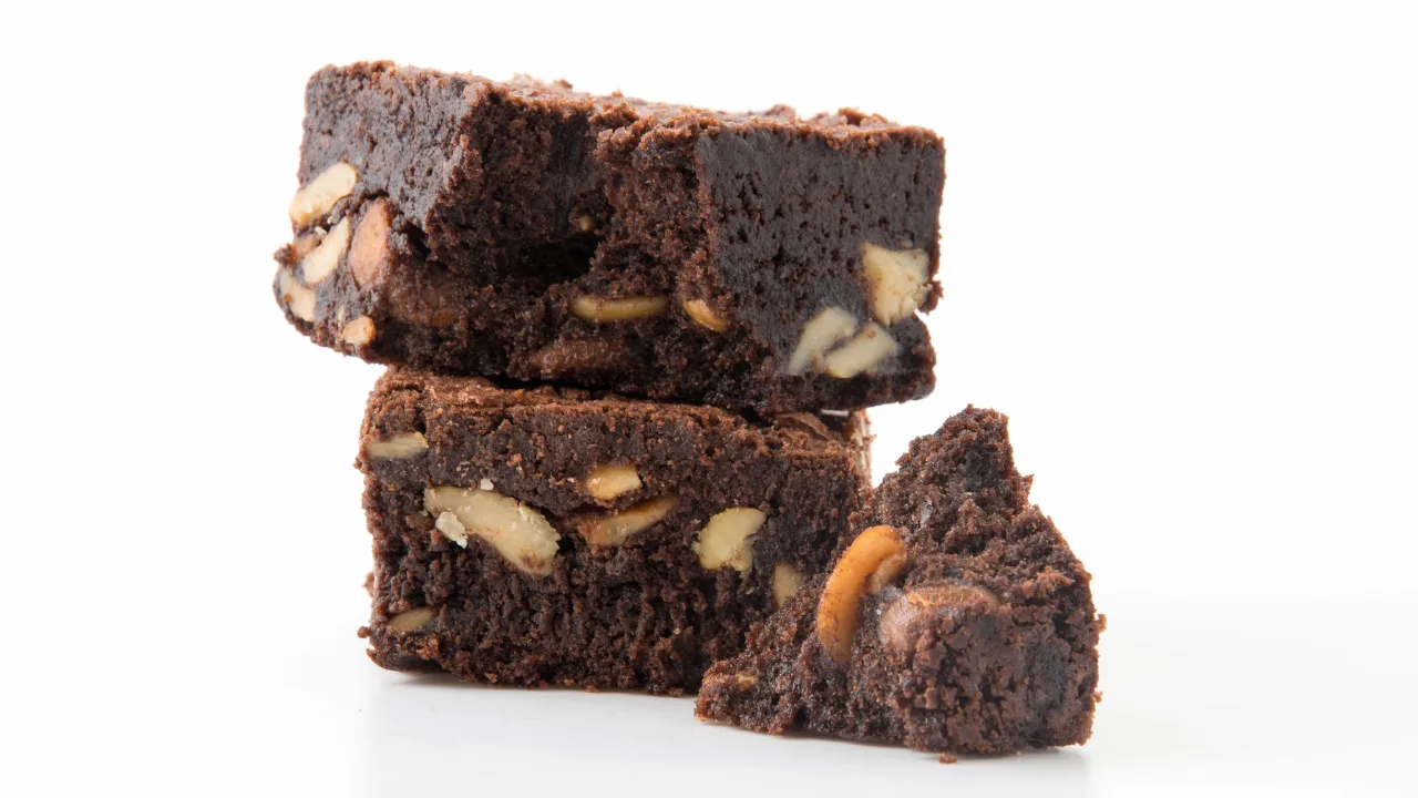 foto de três pedaços de brownie com nozes empilhados sobre fundo branco, destacando a textura densa e os pedaços crocantes de castanhas.