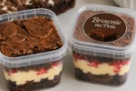 Dois potes transparentes de brownie com camadas de creme de chocolate, um aberto e outro fechado
