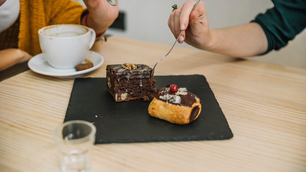 Brownie gourmet sobre prato preto ao lado de xícara de café.