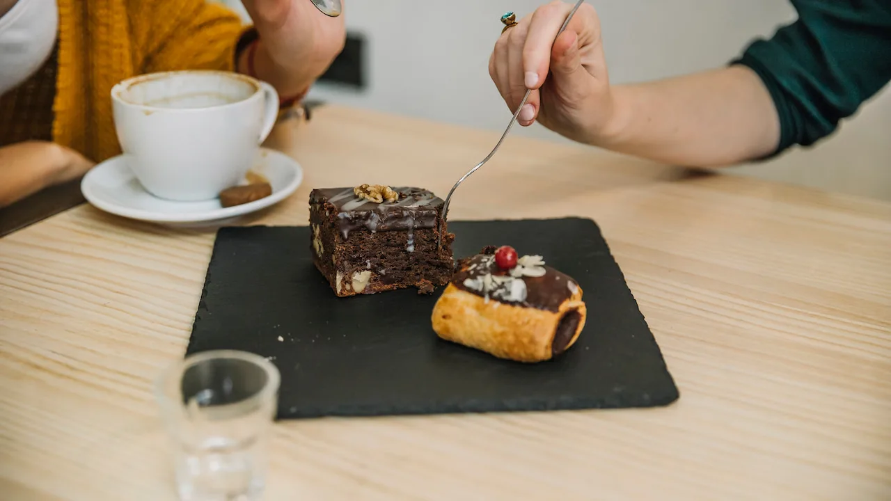 Brownie gourmet sobre prato preto ao lado de xícara de café.
