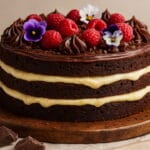 foto de naked brownie decorado com framboesas e flores comestíveis sobre base rústica