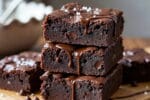 Close-up de brownies saudáveis de chocolate, com calda escorrendo e pedaços de chocolate ao redor.