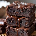 Close-up de brownies saudáveis de chocolate, com calda escorrendo e pedaços de chocolate ao redor.