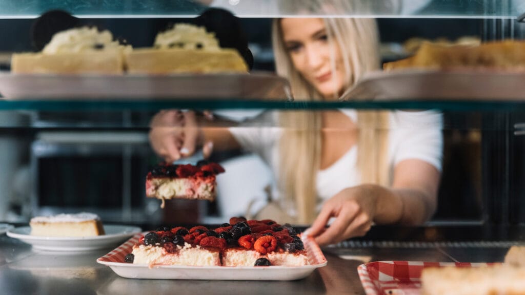 Oportunidade de negócio com confeitaria saudável, mostrando uma dona de negócio servindo uma sobremesa fit em seu estabelecimento.