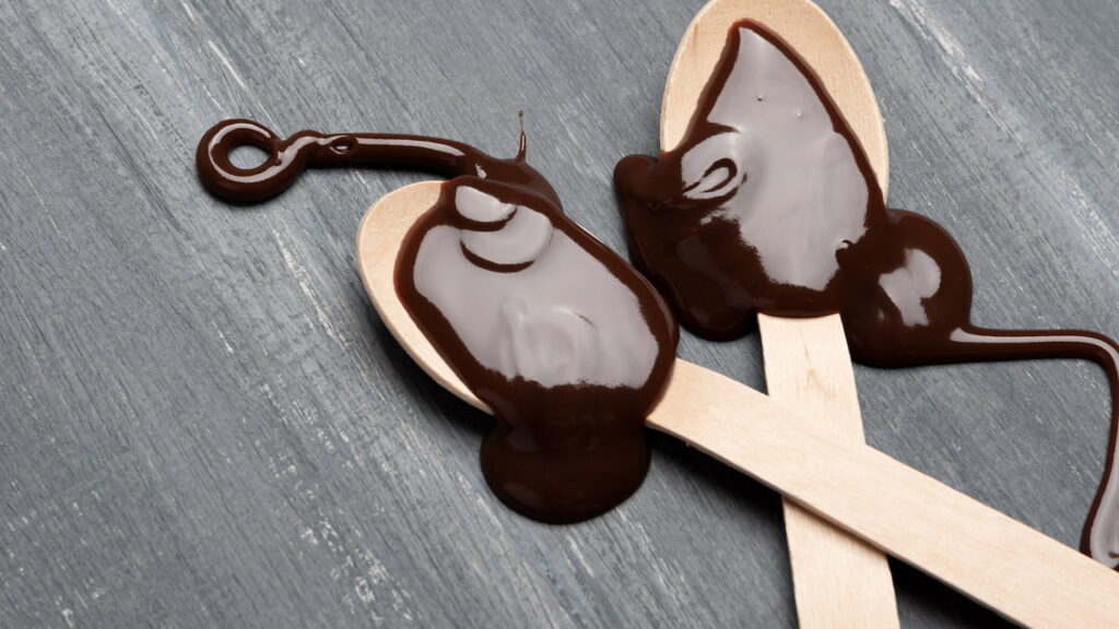 dicas-derreter-chocolate chocolate derretido escorrendo em colheres de madeira sobre superfície escura, ilustrando técnica correta para preparo de brownies