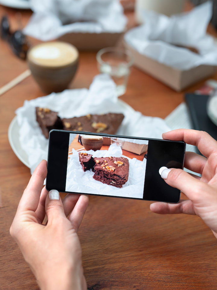 fotografando-bolo-com-celular-para-instagram Mãos tirando foto de uma fatia de bolo com o celular para marketing no Instagram.
