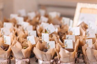 Diversas lembrancinhas com mini brownies embrulhados em papel kraft bege, amarrados com fitas rosadas e decorados com tags personalizadas, organizados sobre uma mesa, relacionadas ao tema lembrancinhas com mini brownies para eventos especiais