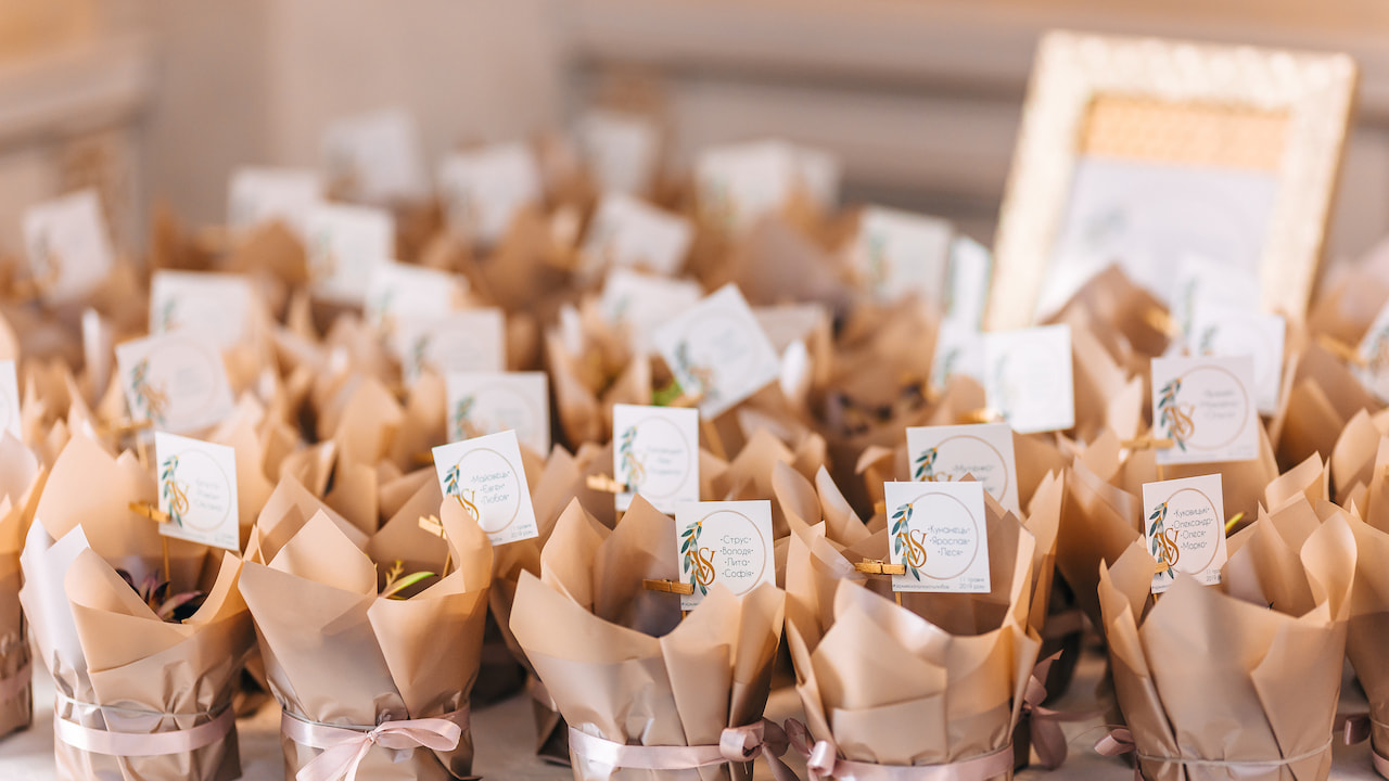 Diversas lembrancinhas com mini brownies embrulhados em papel kraft bege, amarrados com fitas rosadas e decorados com tags personalizadas, organizados sobre uma mesa, relacionadas ao tema lembrancinhas com mini brownies para eventos especiais