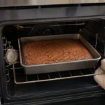 Brownie assando em forma retangular no centro do forno, com termômetro ao lado
