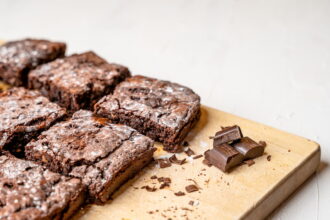 Brownies de chocolate sem ovos com superfície crocante e interior úmido dispostos sobre tábua de madeira ao lado de pedaços de chocolate em barra