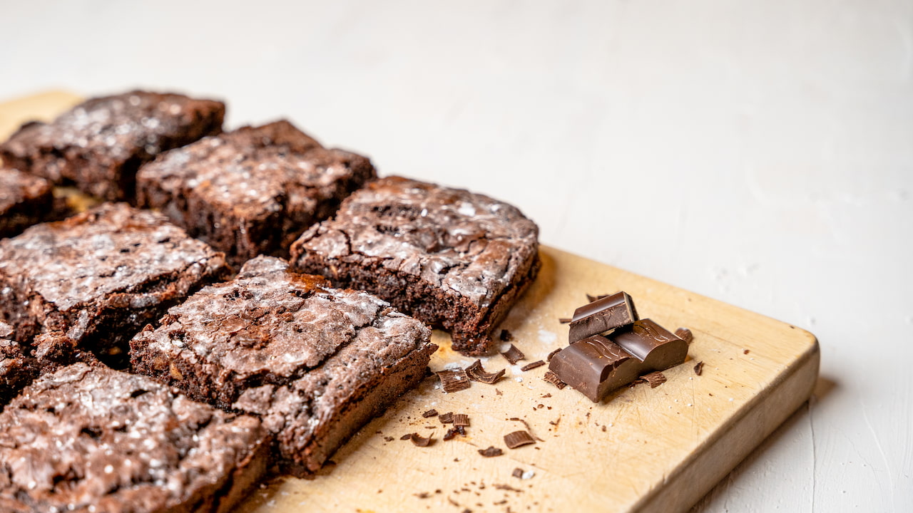 Brownies de chocolate sem ovos com superfície crocante e interior úmido dispostos sobre tábua de madeira ao lado de pedaços de chocolate em barra