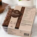 Brownie artesanal embalado com rótulo detalhado, tabela nutricional e alergênicos sobre bancada clara.