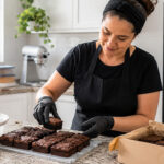 Confeiteira caseira organiza brownies em cozinha limpa, referência a alvará sanitário para confeitaria MEI