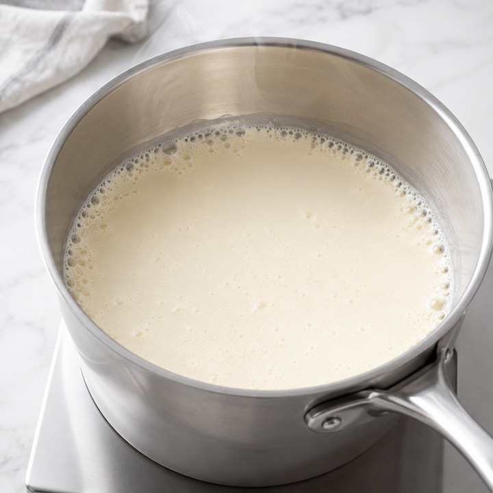 Creme aquecido na panela com bolhinhas nas bordas, mostrando o ponto certo antes de ferver para a ganache.