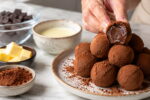 Trufas de chocolate com centro cremoso, cacau em pó e quatro ingredientes da receita profissional na bancada.